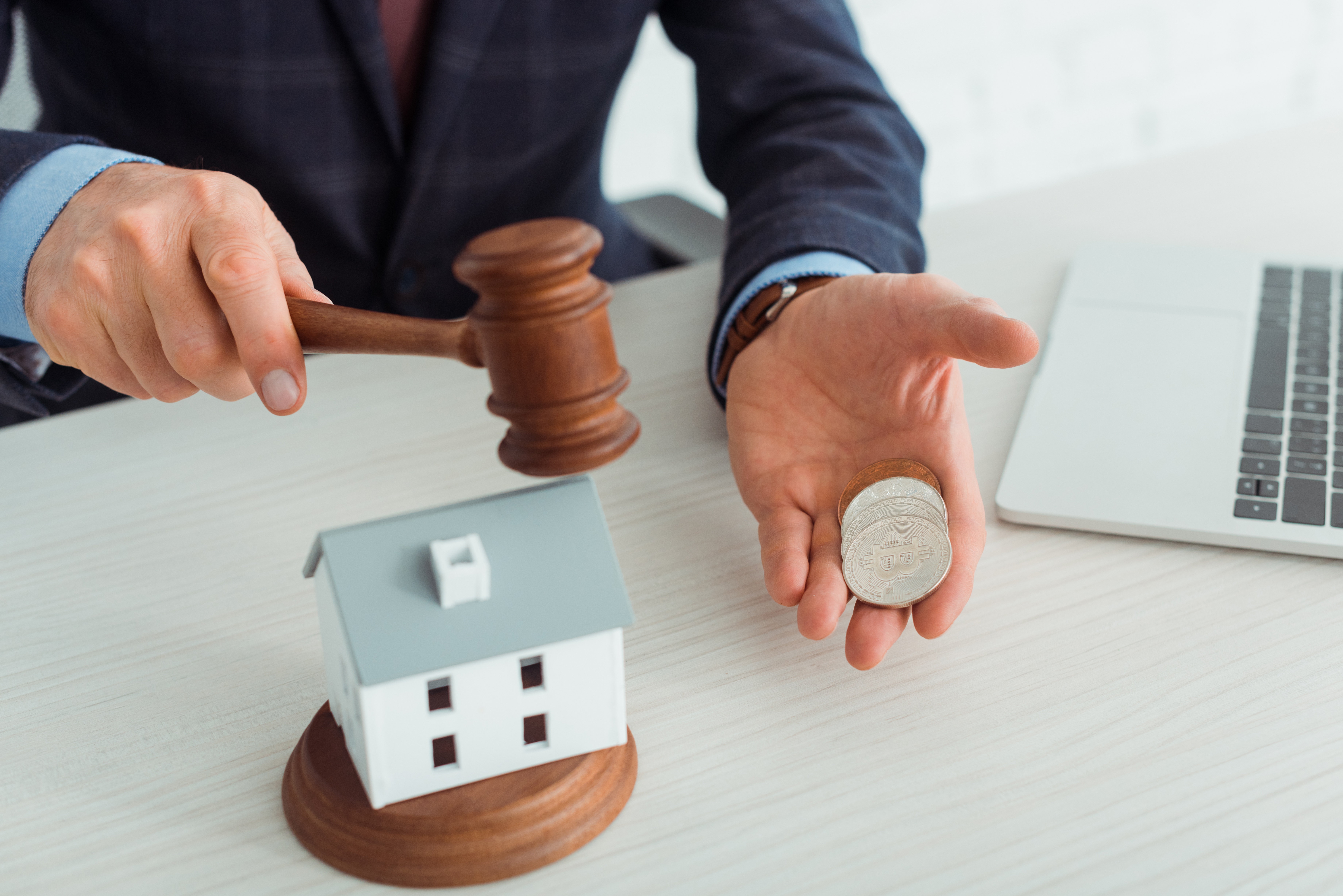 cropped view of auctioneer hitting model of house with gavel and holding coins