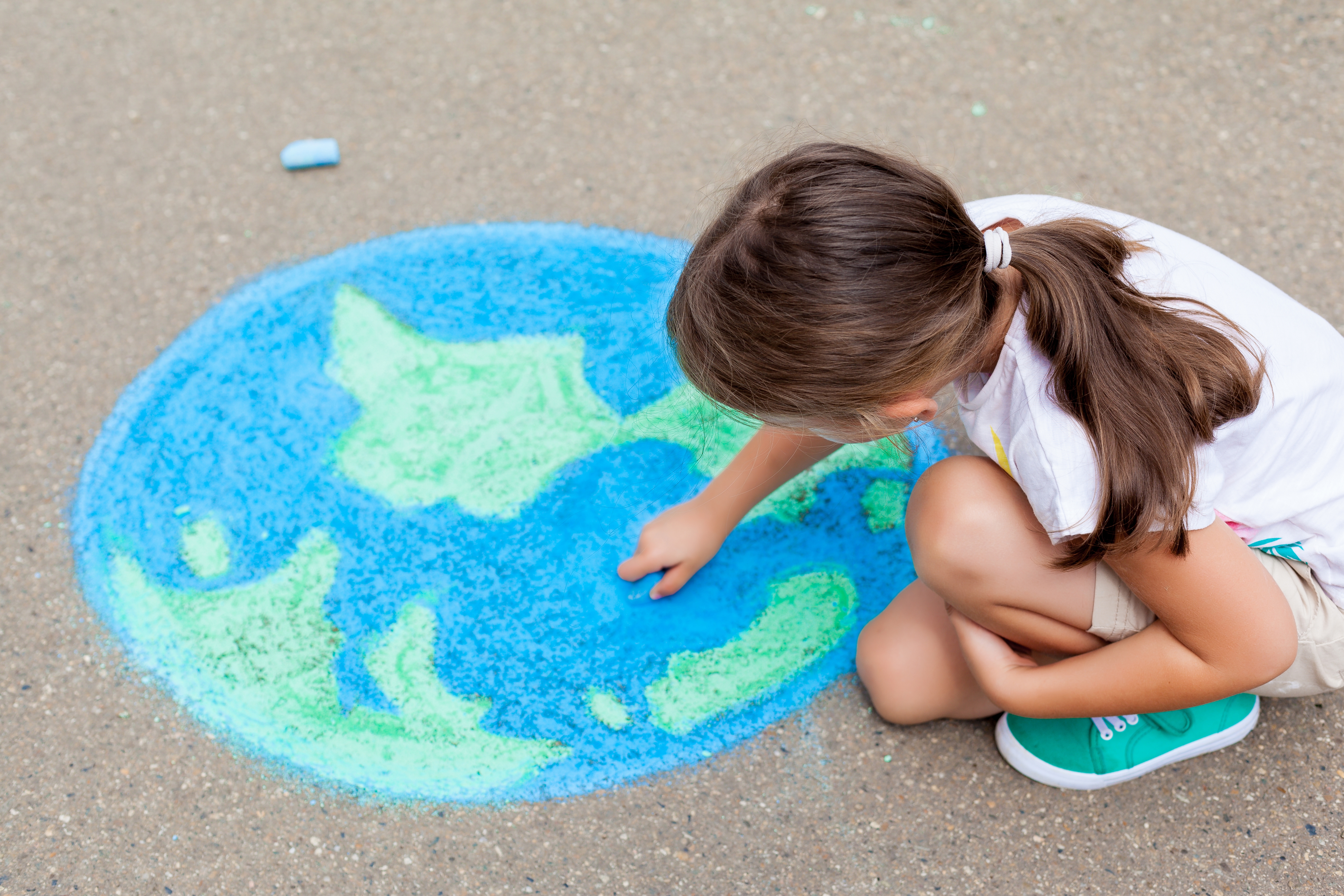 the child girl draws a globe with a map of the world with colored chalk on the asphalt